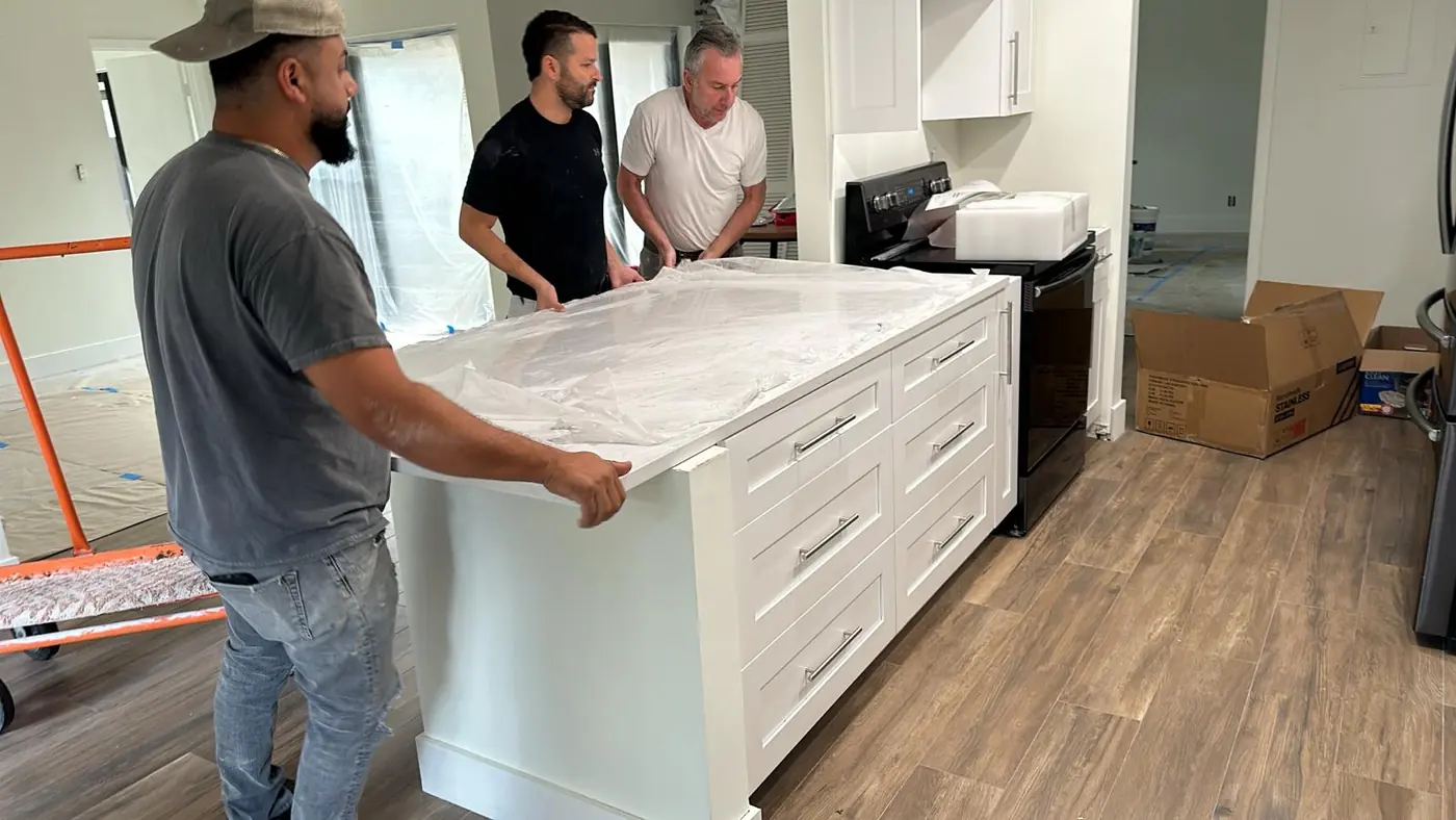 BO Renovation crew setting a white quartz countertop on a kitchen island with white shaker drawers