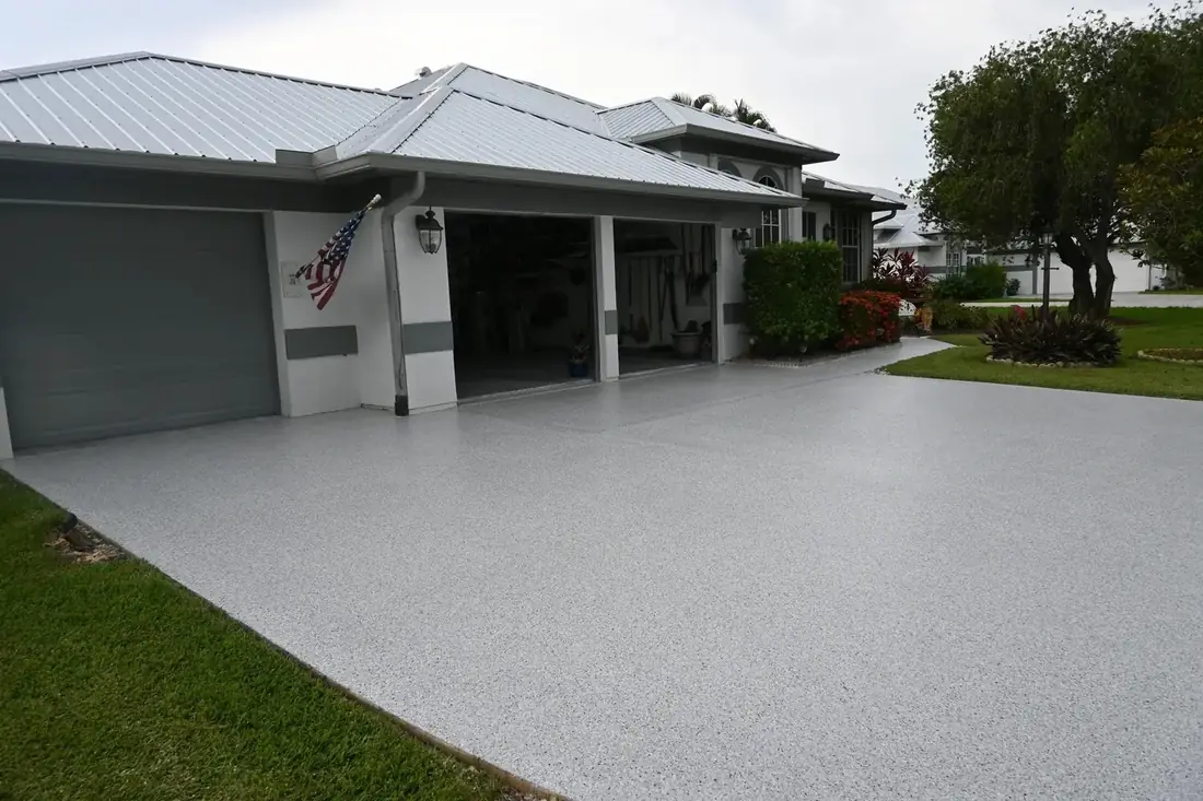 Residential driveway finished with a light gray decorative flake coating in front of a three-car garage