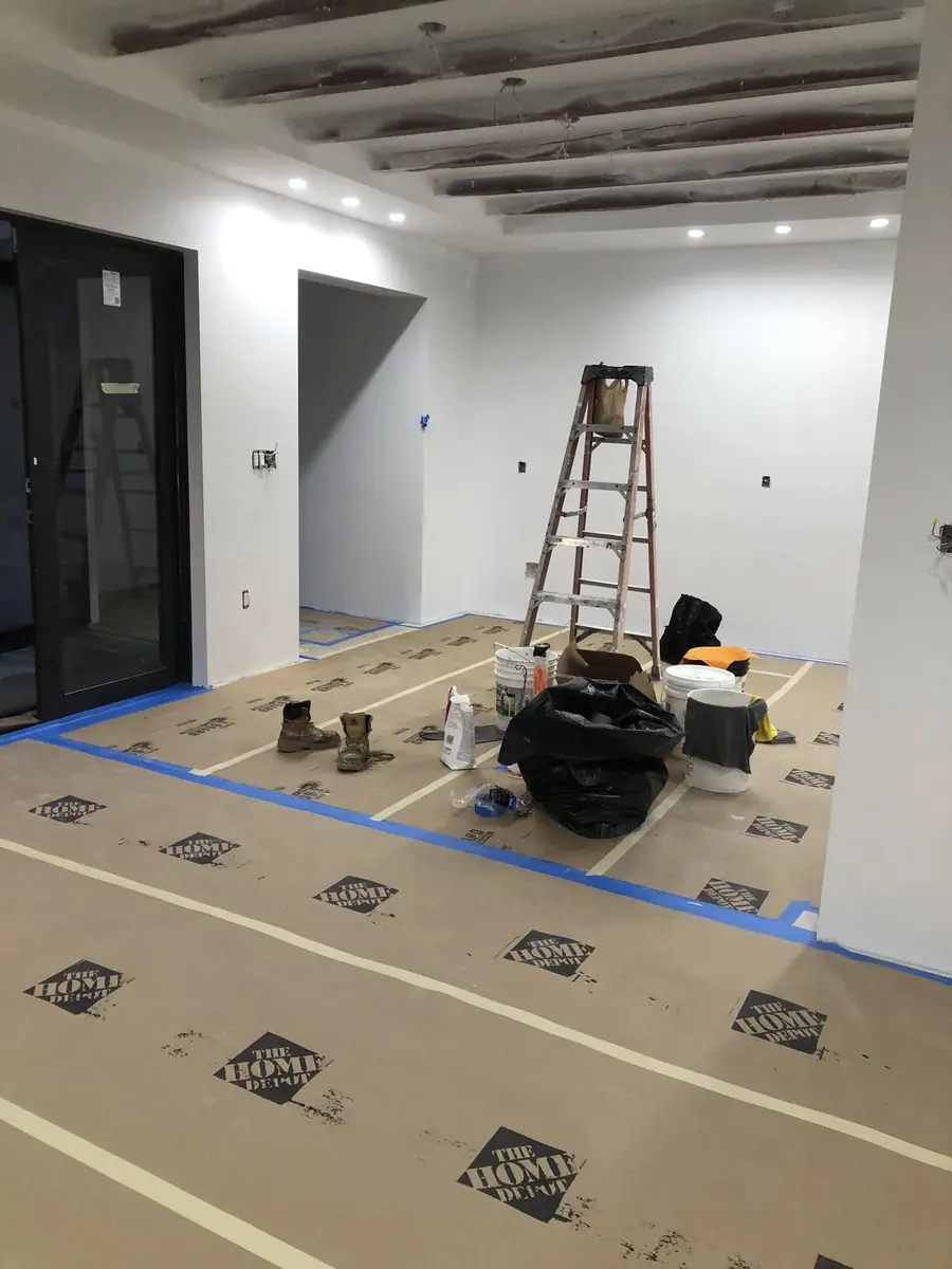 Bright white painted walls and openings with recessed lights, floors covered in protection paper and painting supplies