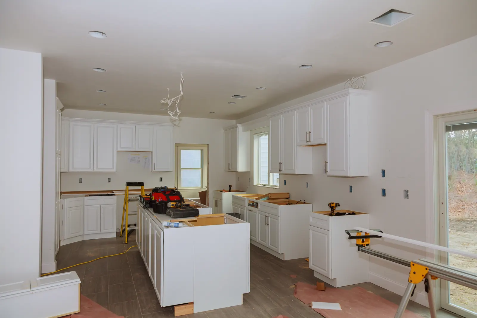 Kitchen renovation in progress, with white cabinets and an island being installed and tools on site