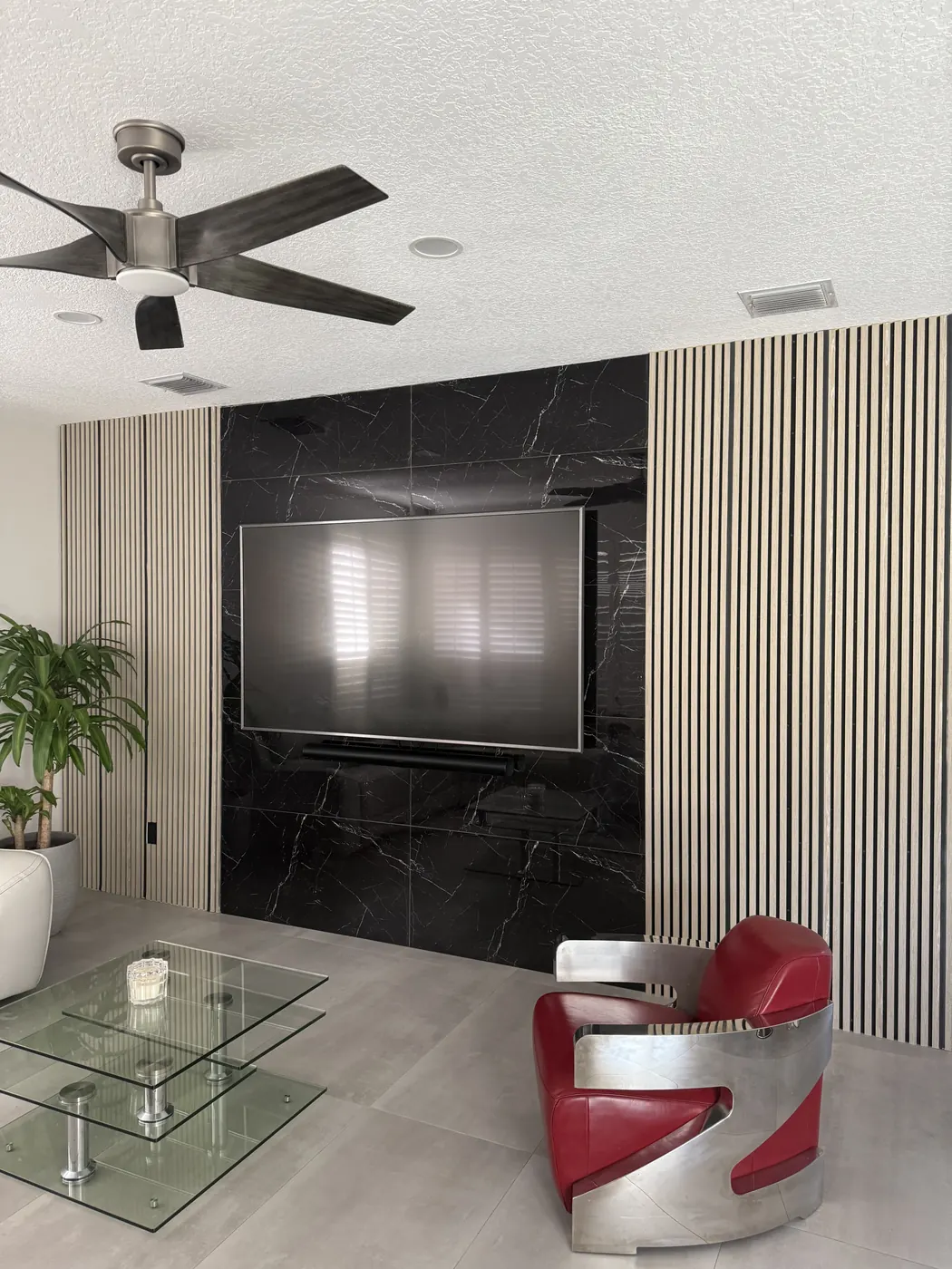 Finished feature wall with black marble-look tile, wall-mounted TV and soundbar, framed by wood slat panels