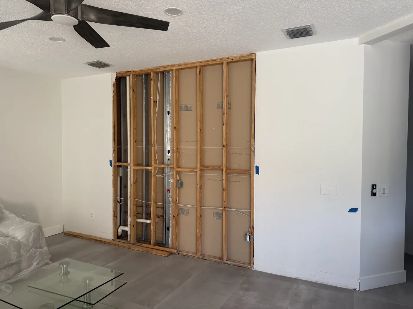 Living room wall opened to the wood framing, exposing plumbing and electrical