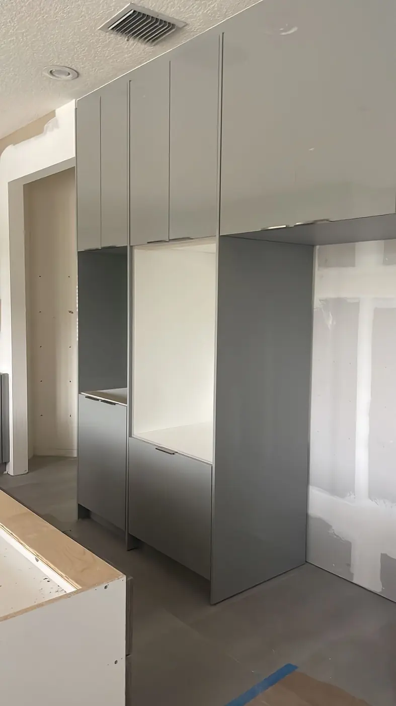 Floor-to-ceiling gray high-gloss tall cabinets with openings for a wall oven and refrigerator