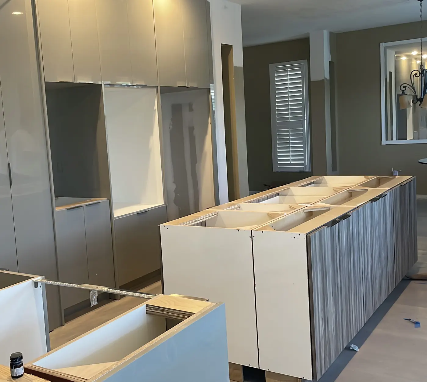 Long kitchen island with wood-grain slab doors being installed in front of tall gray gloss cabinets