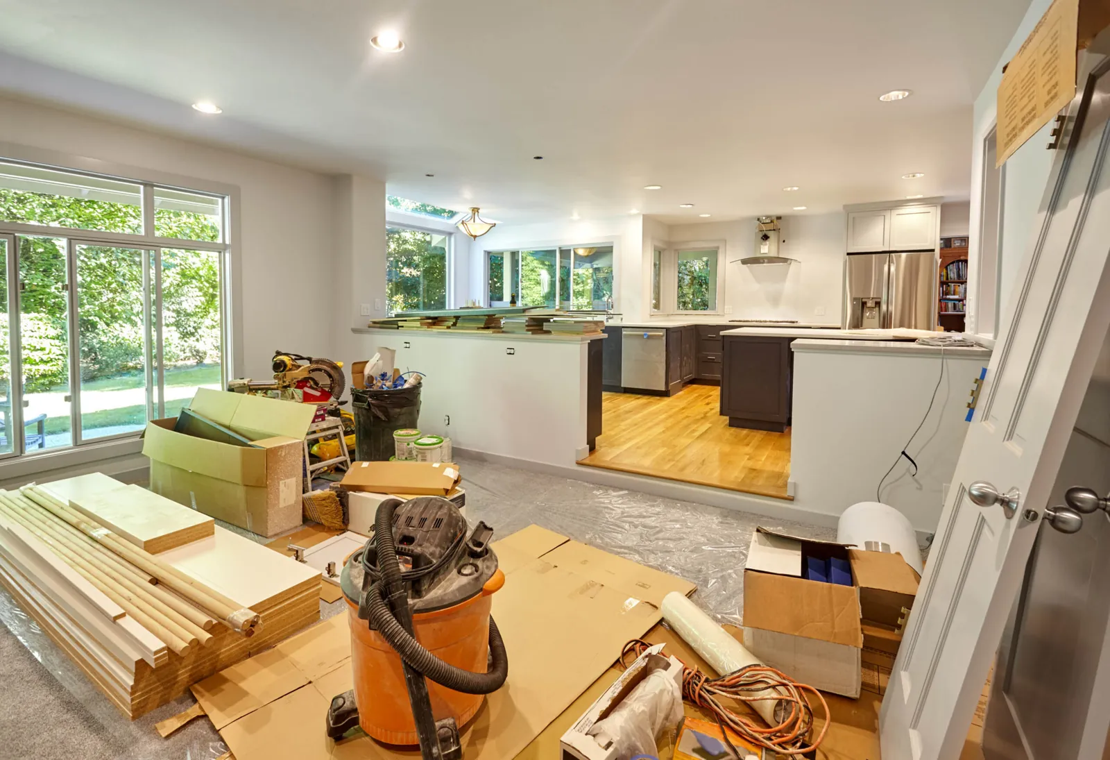 Open-plan home renovation in progress, with a new kitchen installed and trim, cabinets and materials staged in the living area