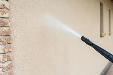 Pressure washer spraying an exterior stucco wall
