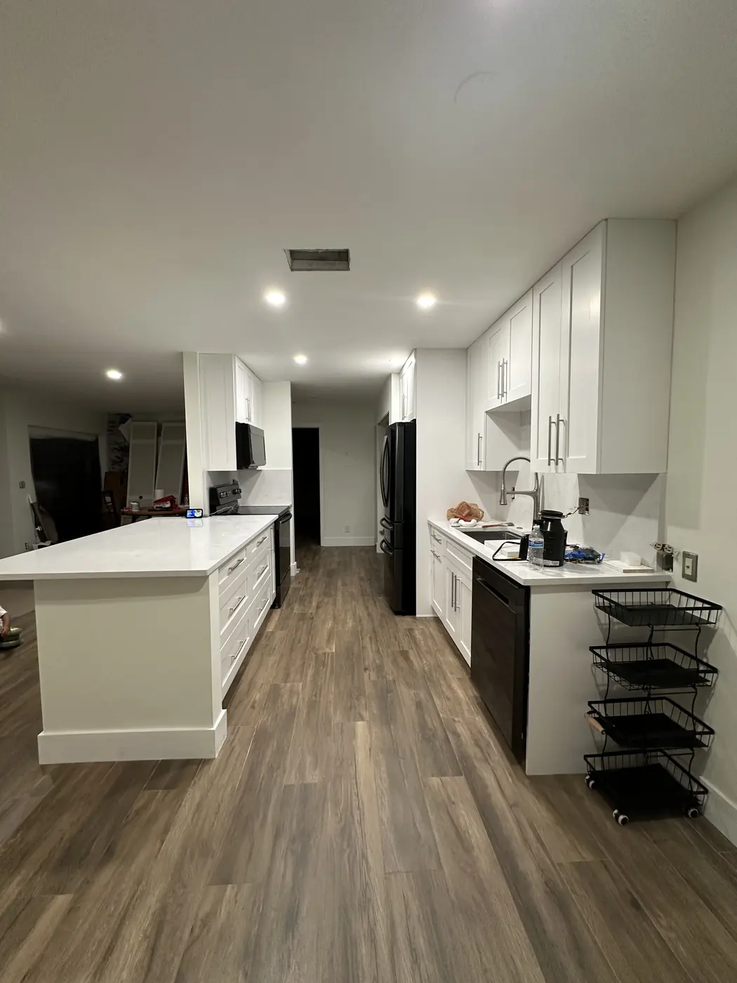 Finished galley kitchen with white shaker cabinets, white quartz countertops and backsplash, black appliances and wood-look tile floor
